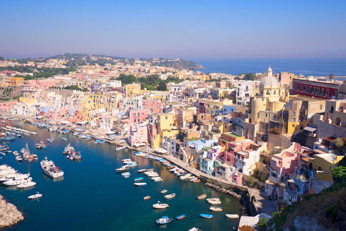 Bambini che giocano sulla spiaggia di Procida, con il mare sullo sfondo e le case colorate, una scena di gioia familiare